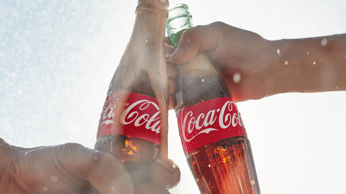 Δύο χέρια που τσουγγρίζουν με δύο μπουκάλια Coca-Cola.