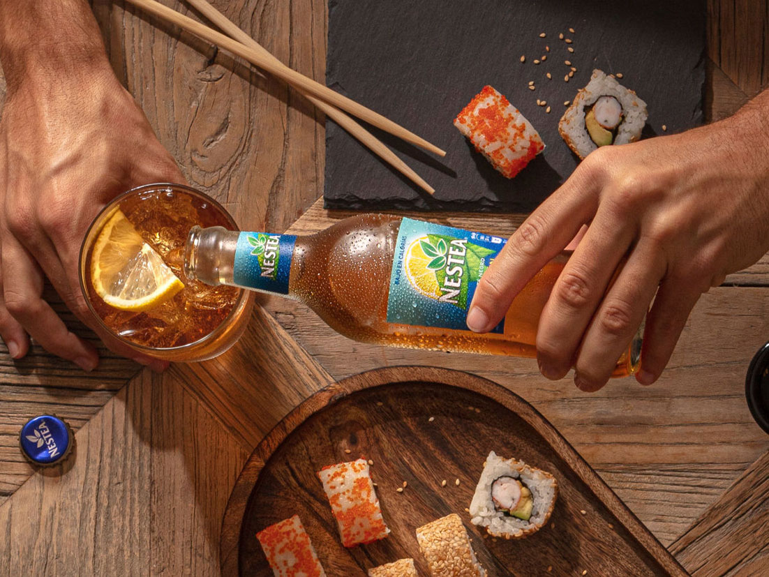 Botella de Nestea llenando un vaso sobre mesa con sushi