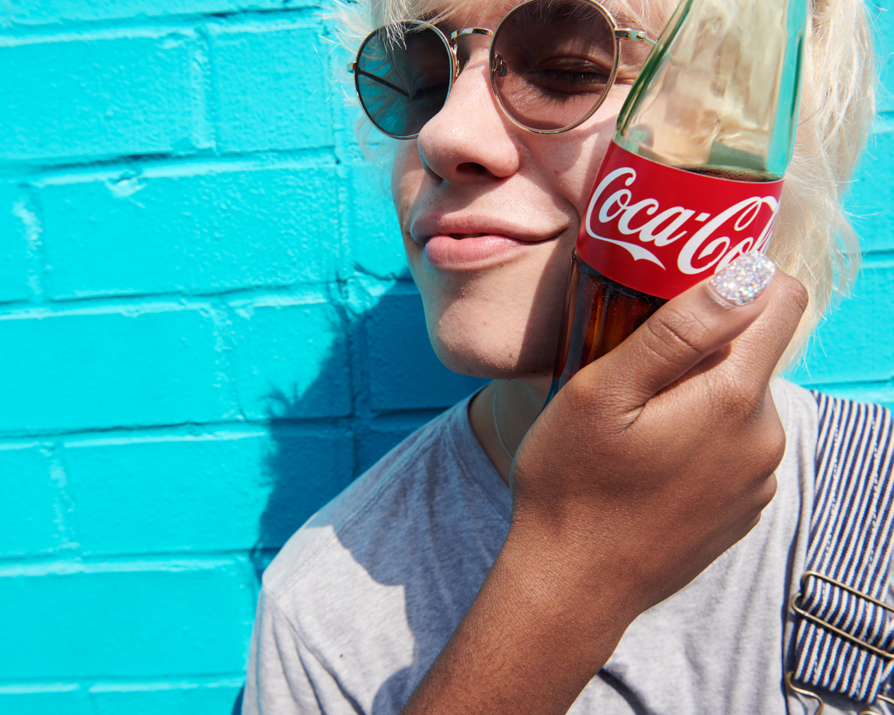 Une femme pose une bouteille de Coca-Cola sur ses joues et profite de son moment de détente