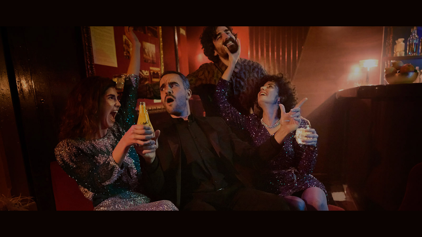 Dva muškarca i dvije žene uživaju na zabavi dok piju Schweppes u zamračenoj prostoriji