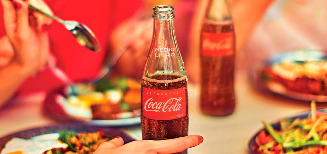 Una mesa servida con comida, refrescos de Coca-Cola y personas conviviendo
