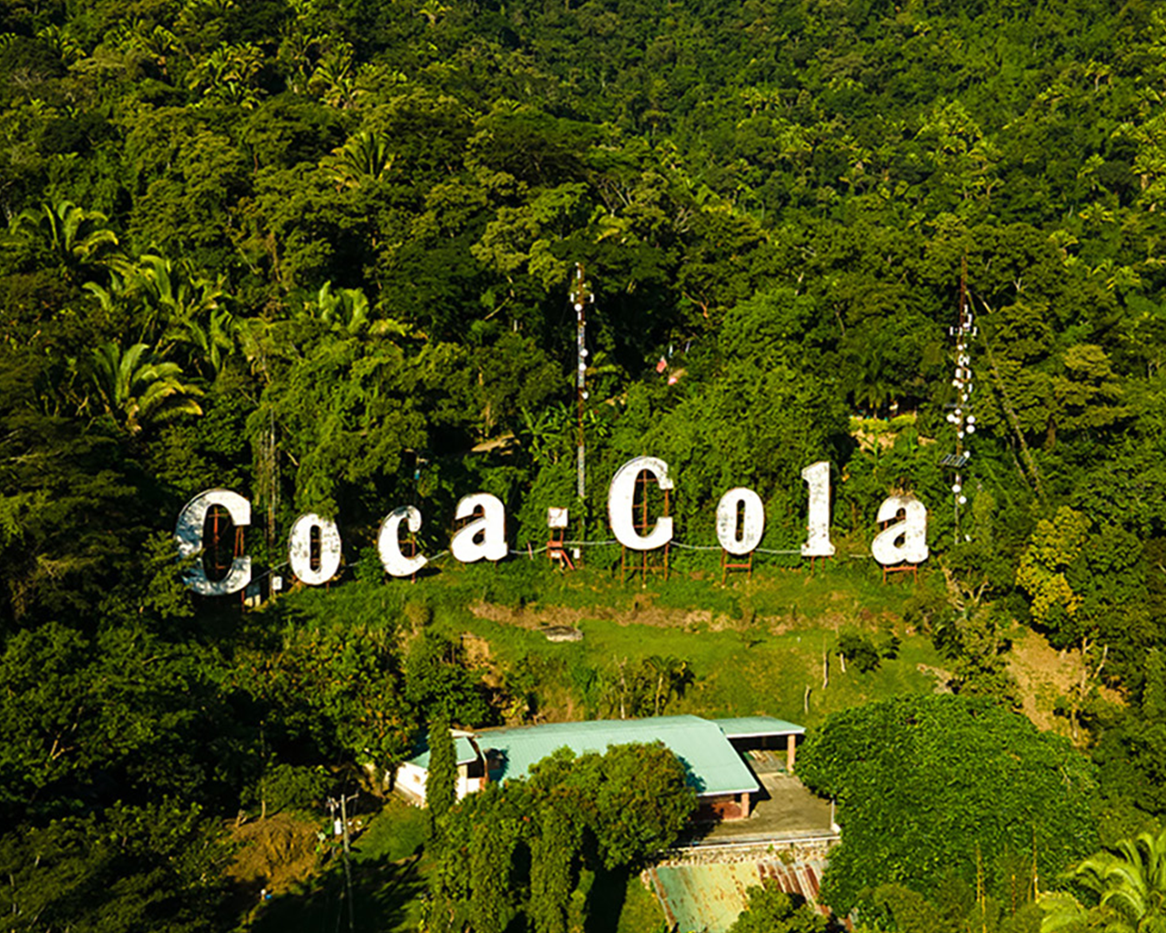Vista aérea de un gran cartel de Coca-Cola en el medio de un frondoso bosque.