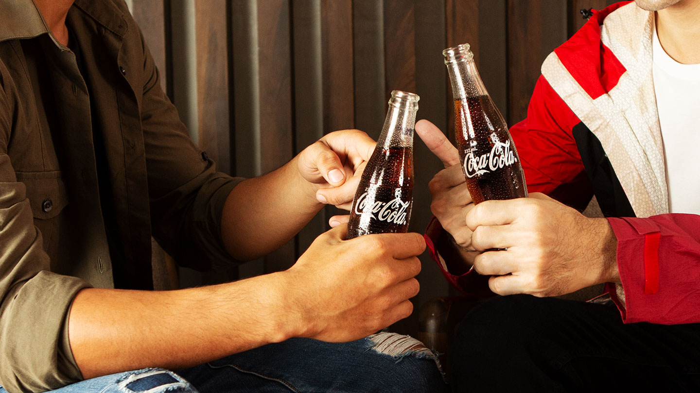  Cropped view of two people toasting with glass bottles of Coca-Cola