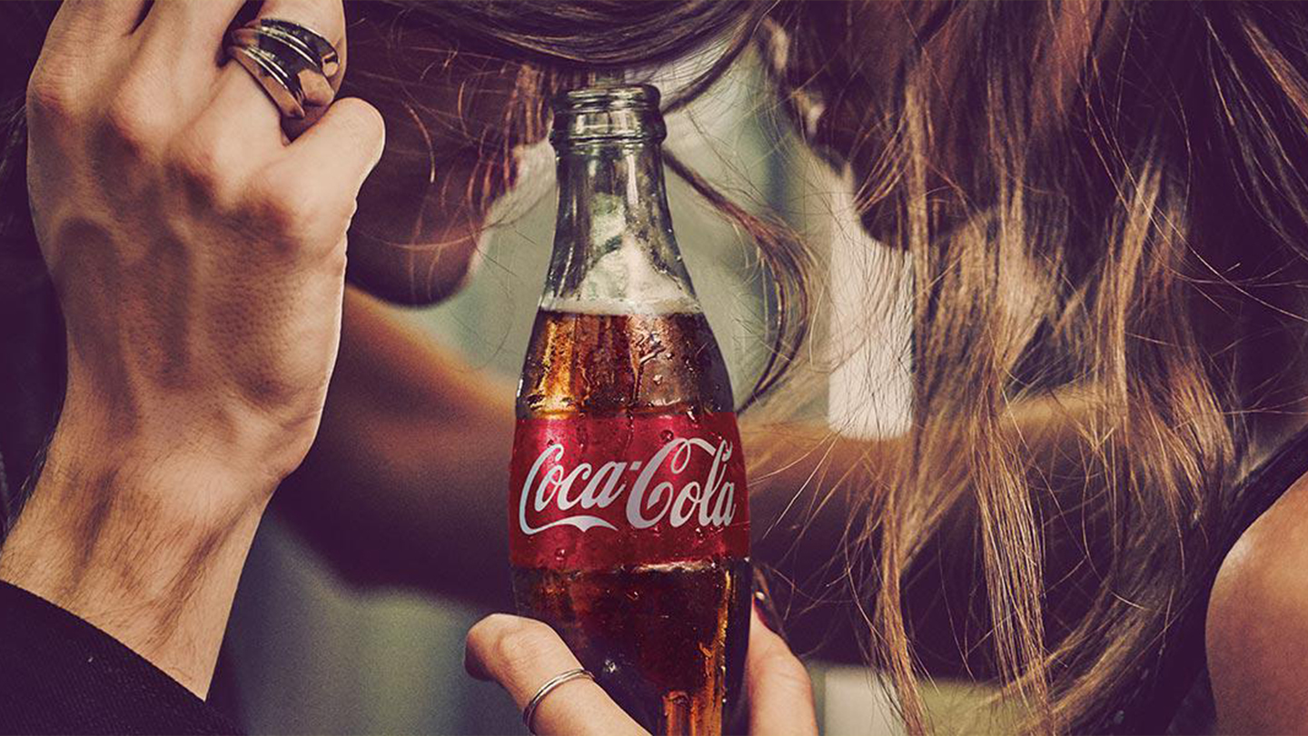 baner sa flašicom Coca-Cole u fokusu i momkom i devojkom sa strana