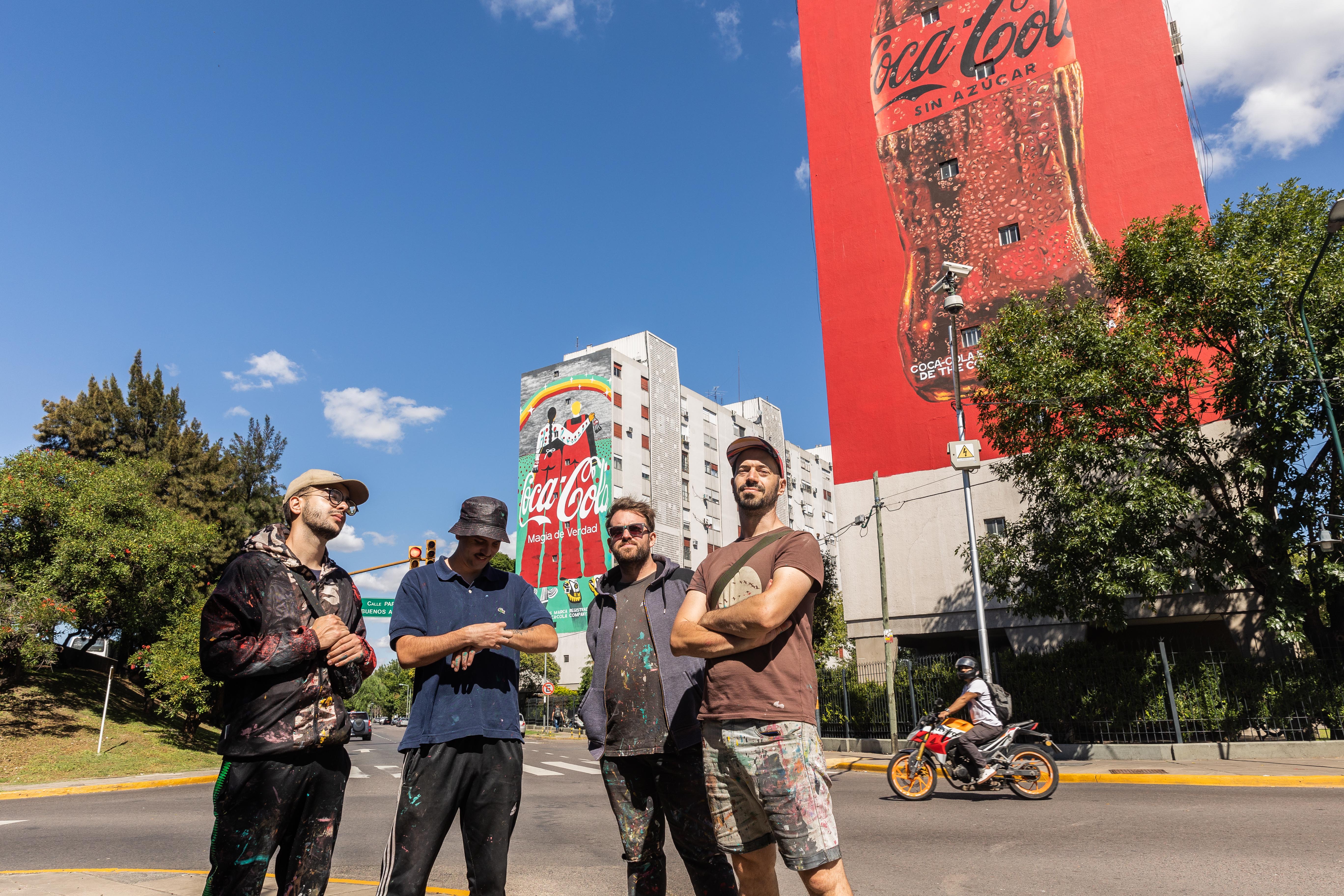 Cuatro hombres con edificios con mural de Coca-Cola de fondo