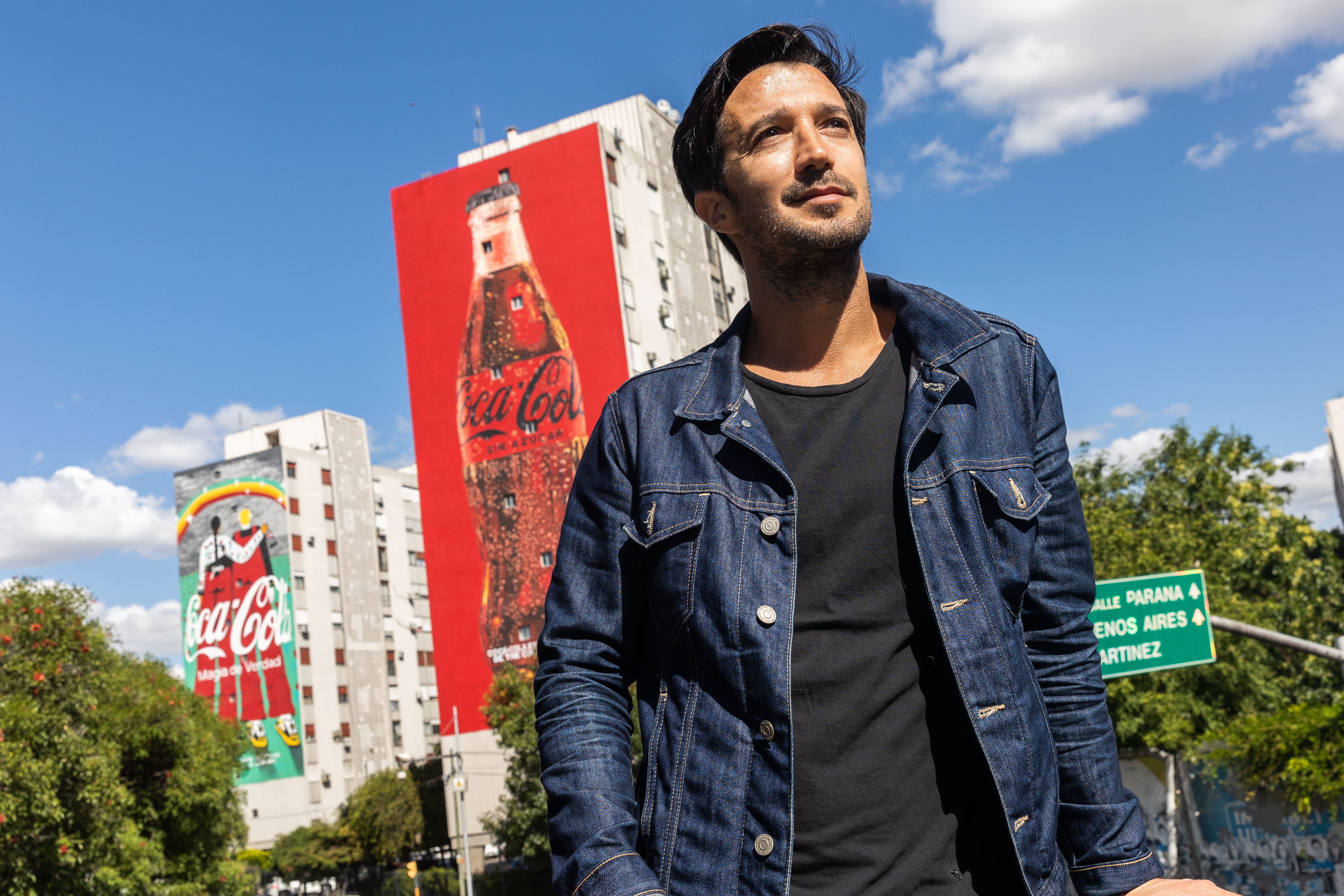 Hombre con dos edificios con mural de Coca-Cola de fondo
