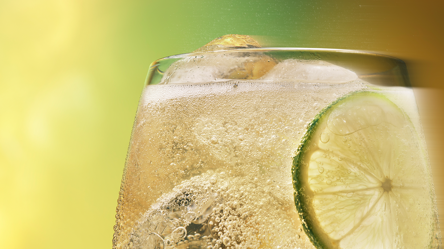 Un Toreador Ginger Ale con cubitos de hielo y una rodaja de lima y limón en un vaso. La bebida está burbujeante y parece refrescante sobre un fondo verde.
