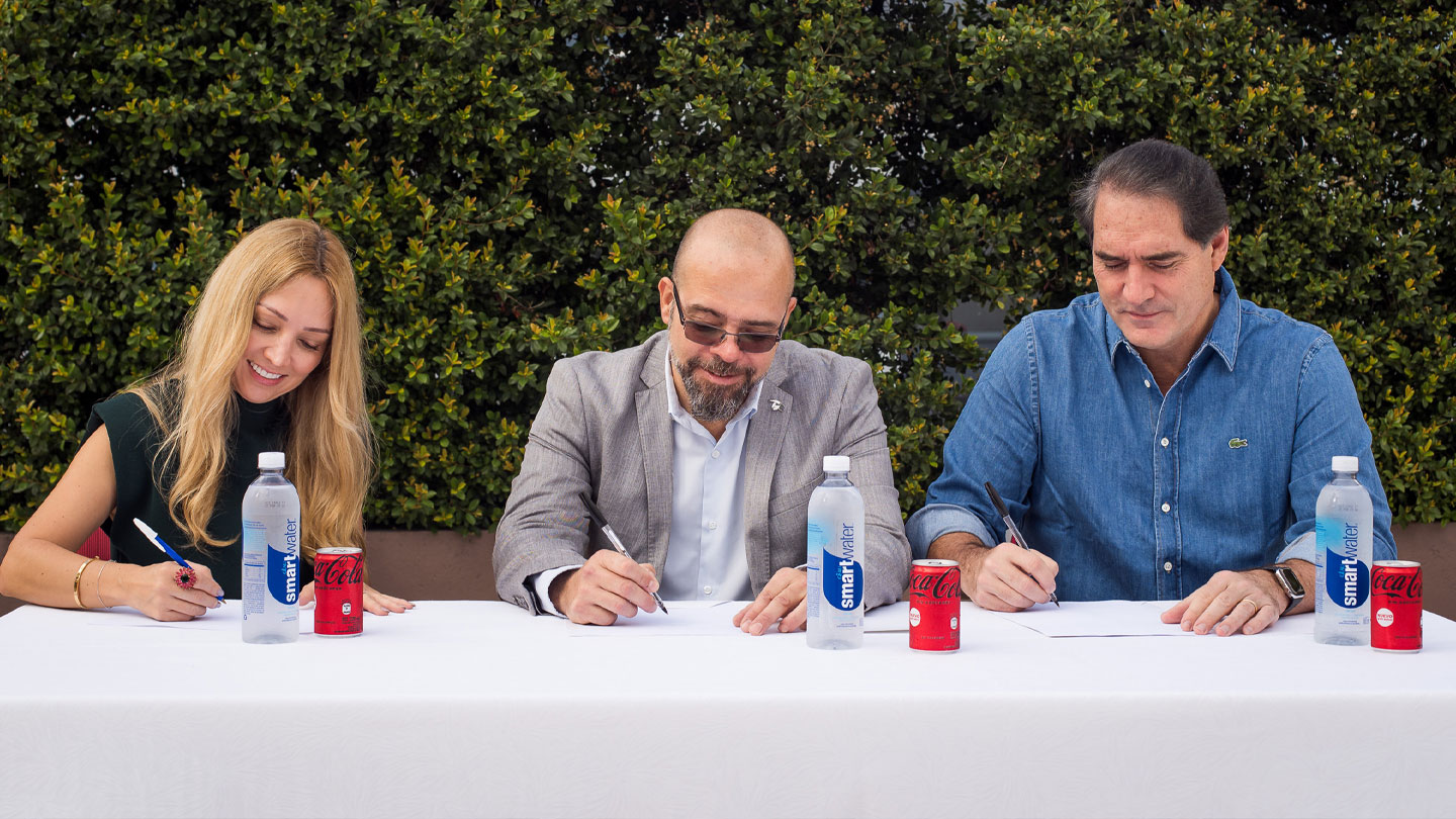 Tres personas sentadas a una mesa firmando un papel