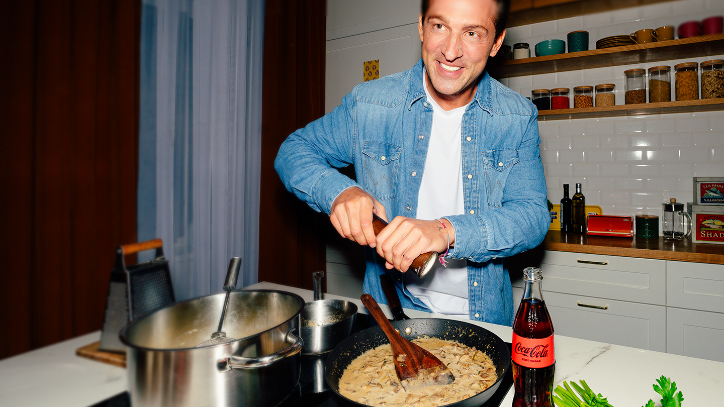 A man and woman, each holding a can of Coke, sit on a safa, laughing.