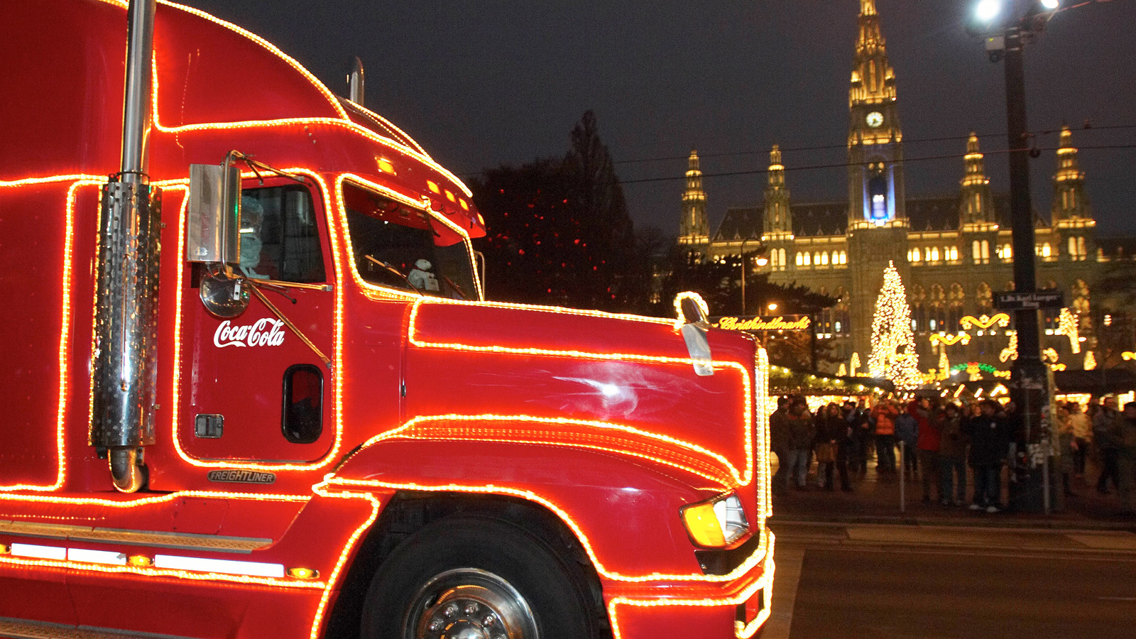Coca-Cola Weihnachtstruck, leuchtend rot, bei Dämmerung vor dem Weihnachtsmarkt auf dem Wiener Rathaus