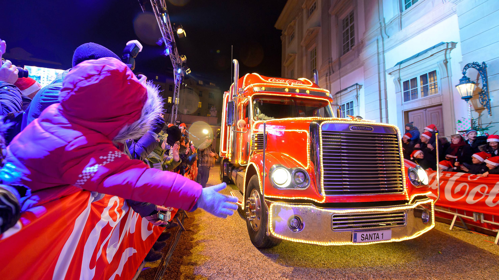Coca-Cola Weihnachtstruck, leuchtend rot, umgeben von freudigen Zuschauern bei Dämmerung