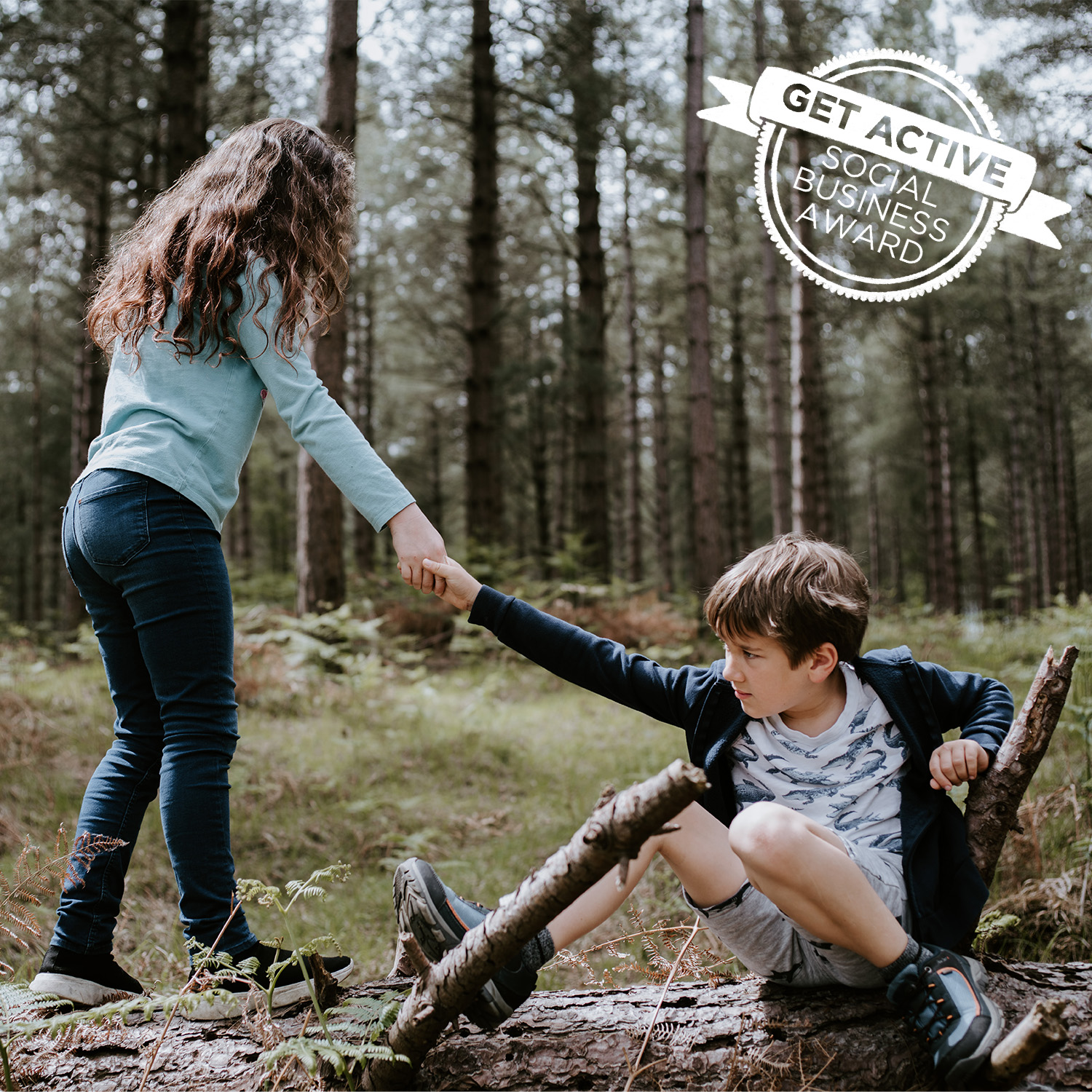 Ein Mädchen reicht einem Jungen, der am Baumstamm im Wald sitzt, die Hand und hilft ihm auf.