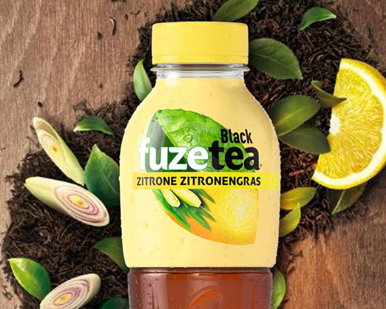 Eine Flasche FuzeTea Schwarzer Tee-Zitrone-Zitronengras, im Hintergrund Zitronenschnitz und Blätter