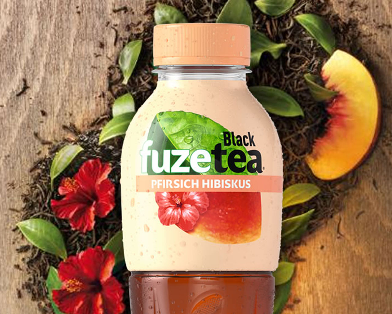 Eine Flasche FuzeTea Schwarzer Tee Pfirsich-Hibiskus, im Hintergrund Pfirsichschnitz und Hibiskusblüten