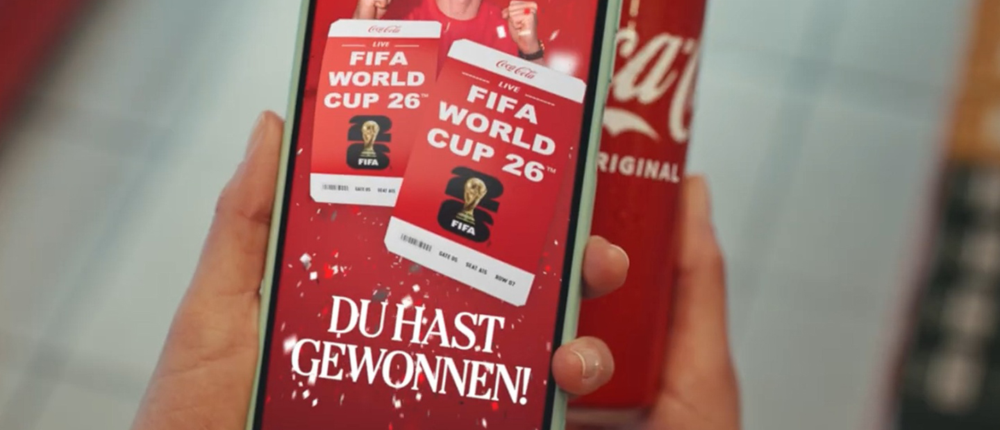 Hand hält ein Smartphone mit der Coca-Cola App, auf dem der Gewinn von Tickets für die FIFA World Cup 2026™ angezeigt wird; im Hintergrund ist eine Coca-Cola Dose zu sehen.