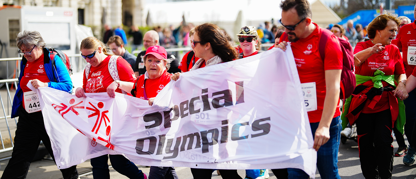 Teilnehmer:innen des Coca-Cola Inclusion Run laufen gemeinsam durch Wien und tragen ein „Special Olympics“-Banner.