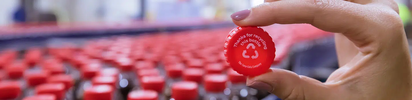 A woman's hand holding a recyclable Coca-Cola bottle cap