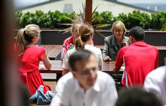 A group of people having a conversation in a external area with refectory tables