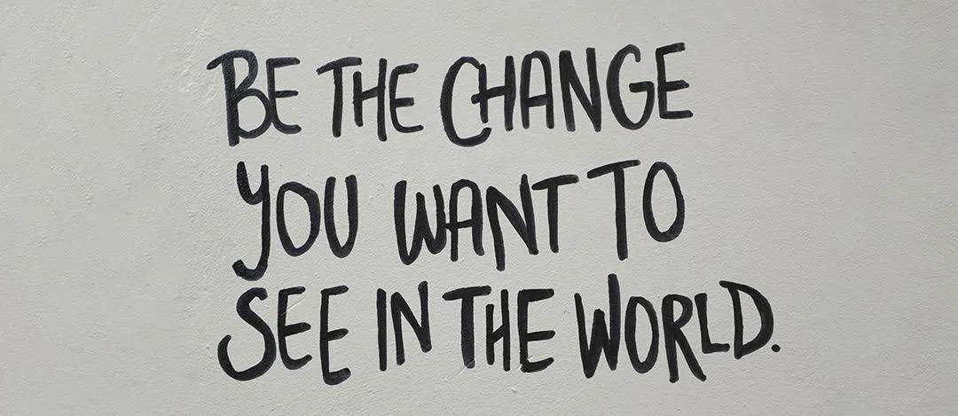 A sentence written on a wall with black ink says 'Be the change you wan to see in the world.'