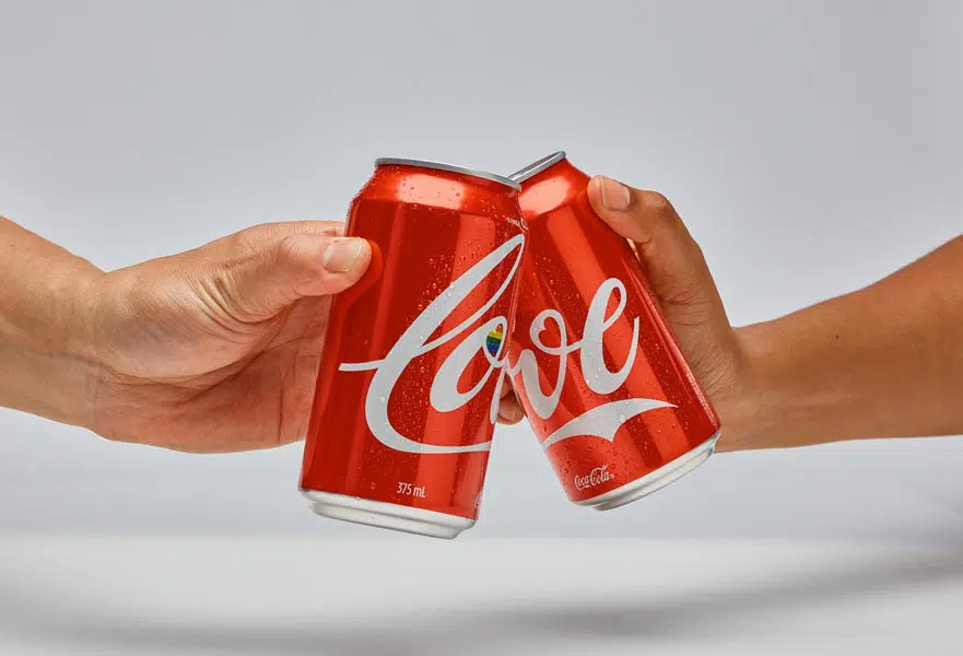 Two hands doing a toast with Coca-Cola cans with the word 'Love' printed on them