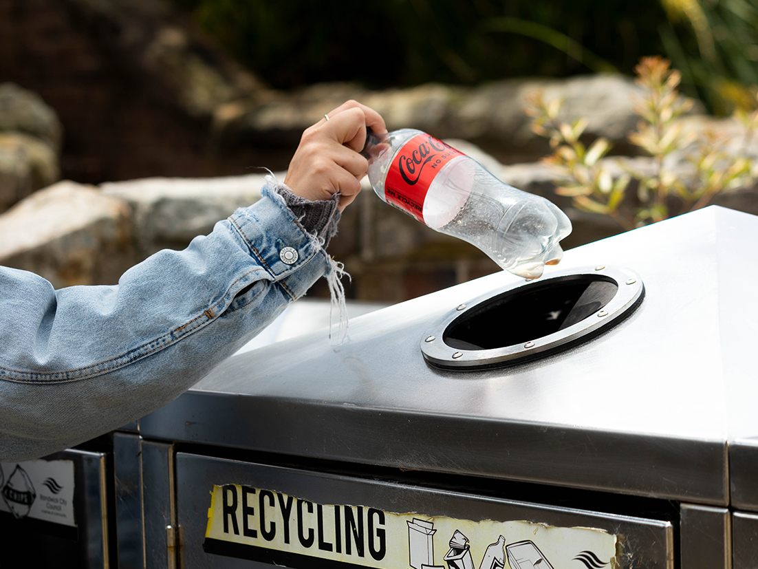 Man putting an empty Coca-Cola bottle in a recyclabe container