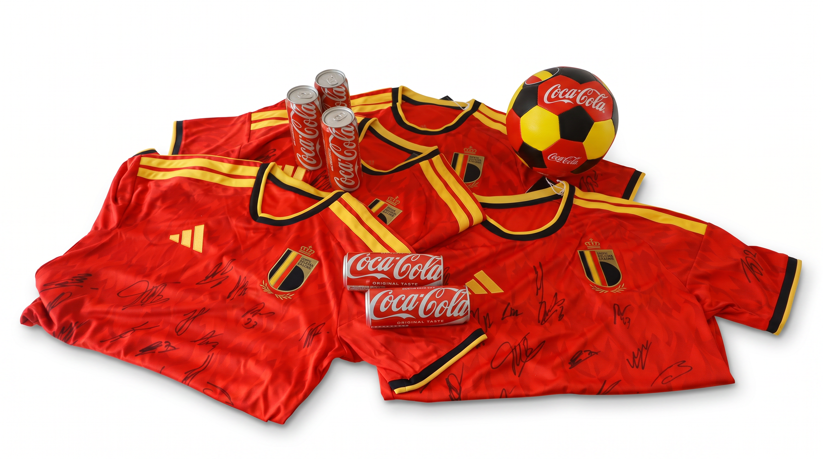 Maillots de football belges rouges signés, disposés sur fond blanc, accompagnés de plusieurs canettes de Coca‑Cola et d’un ballon aux couleurs de la Belgique avec le logo Coca‑Cola.