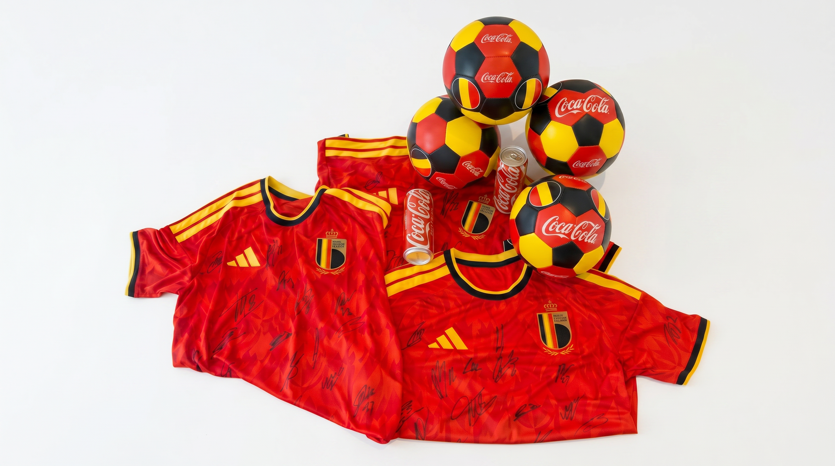 Deux maillots rouges de l’équipe de Belgique, couverts de signatures, sont disposés sur un fond blanc avec plusieurs ballons de football Coca‑Cola rouge, jaune et noir, ainsi que deux canettes de Coca‑Cola. L’ensemble présente une composition promotionnelle sportive aux couleurs nationales belges.