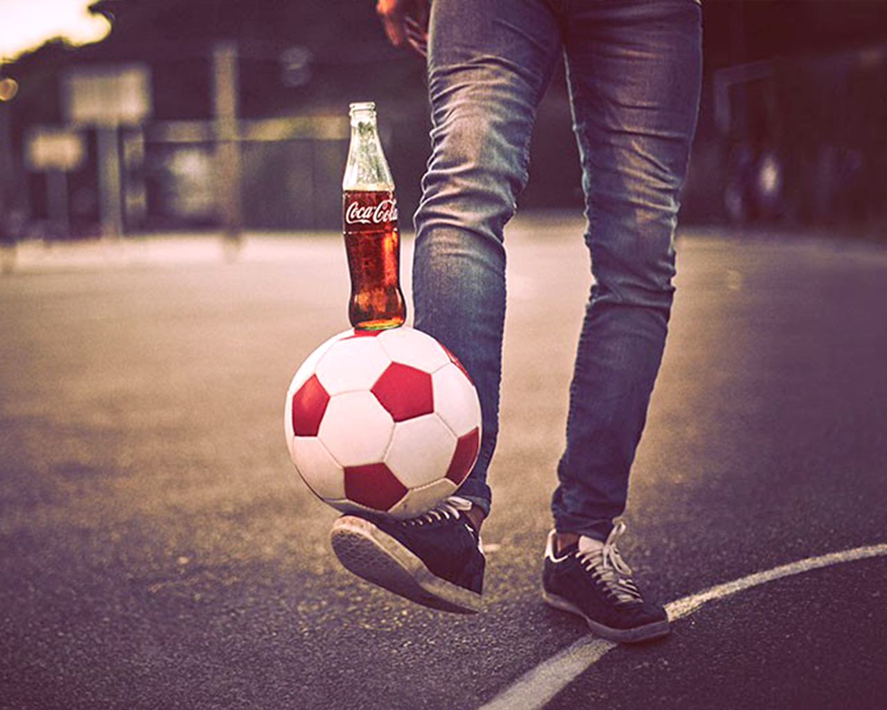 Een man die een voetbal op zijn voet houdt en een Coca-Cola fles op de voetbal plaatst