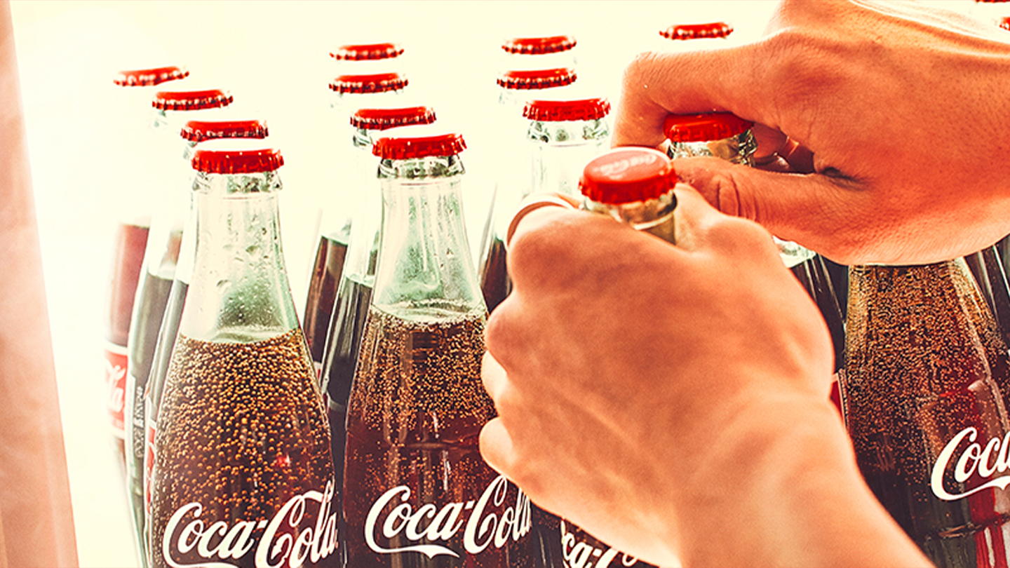Unas manos sacando botellas de Coca-Cola de un refrigerador