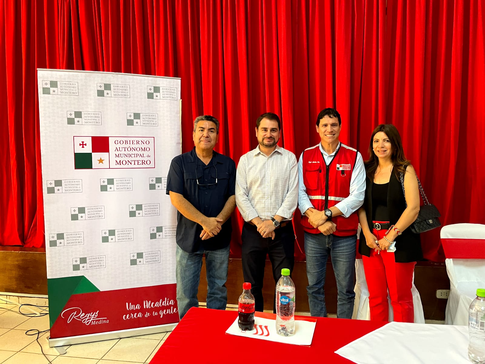 Cuatro personas posan con telón rojo de fondo