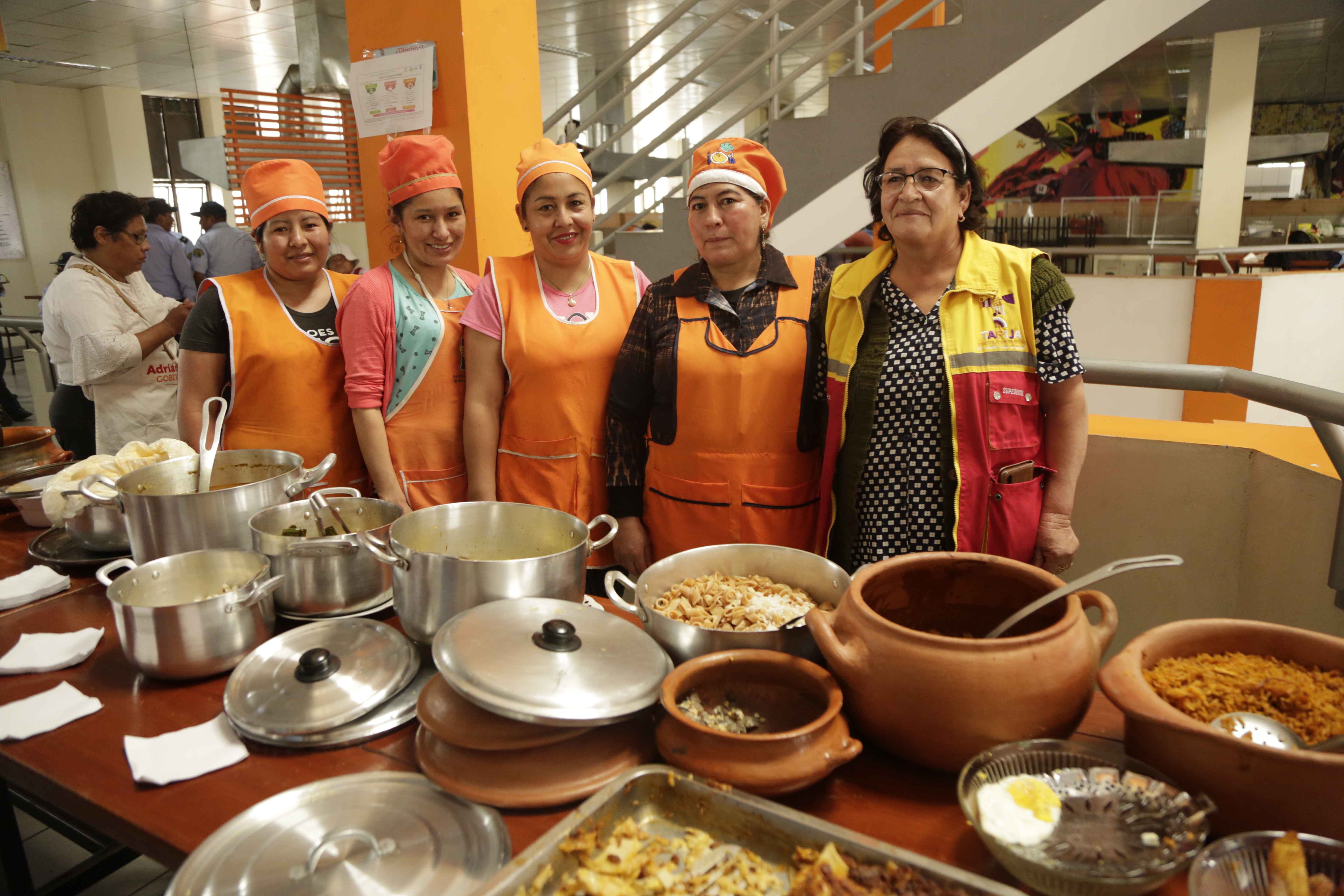 Cinco cocineras posan delante de ollas con comida