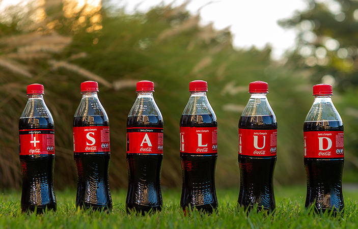 Seis etiquetas de botellas de Coca-Cola forman la frase "+ SALUD"