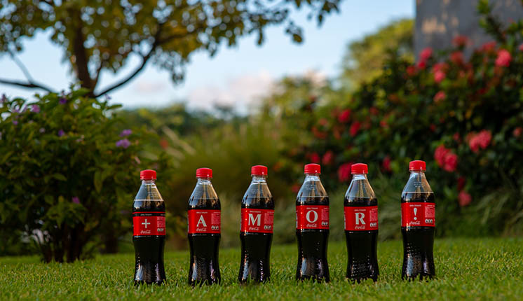 Seis etiquetas de botellas de Coca-Cola forman la frase "+ AMOR!"