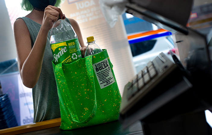 Una mujer en la caja de un supermercado, utiliza un colorido bolso de la marca Sprite