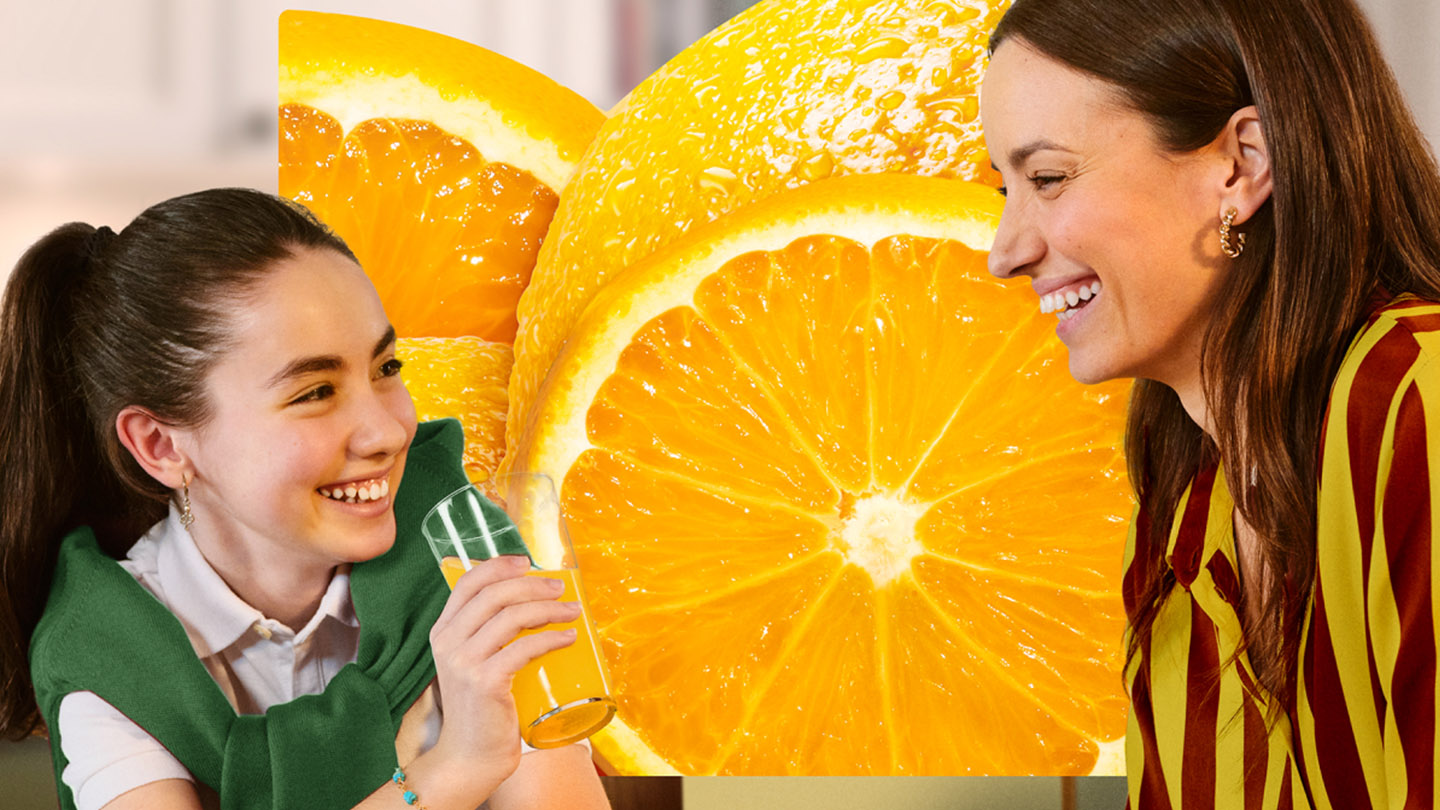 Duas mulheres riem juntas em frente a imagem de uma laranja