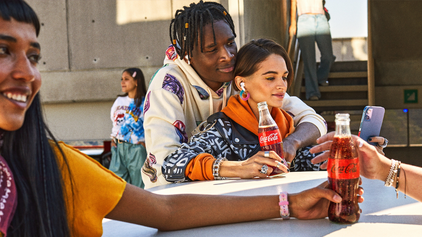 Casal de jovens adultos sentados juntos apreciando Coca-Cola e socializando ao ar livre.