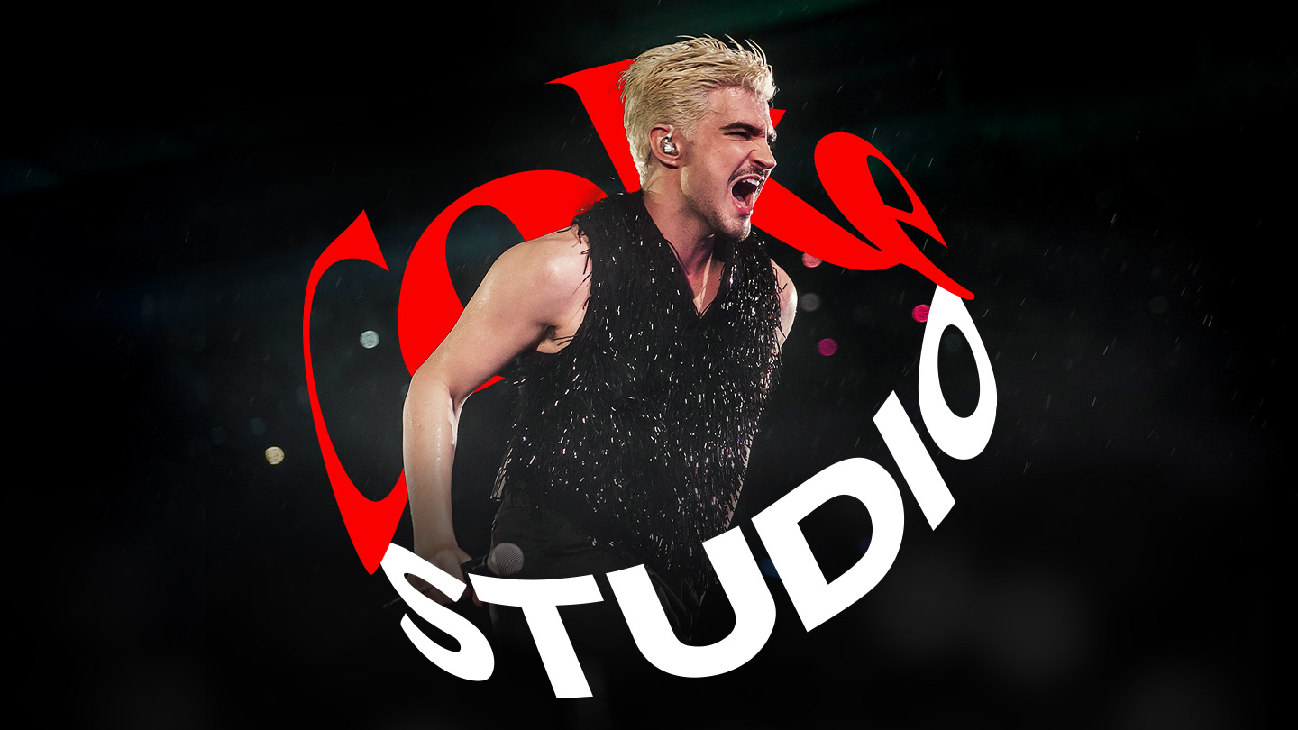 O cantor brasileiro Jão cantando, segurando um microfone na mão, cercado pelo logo do Coke Studio com um fundo preto.