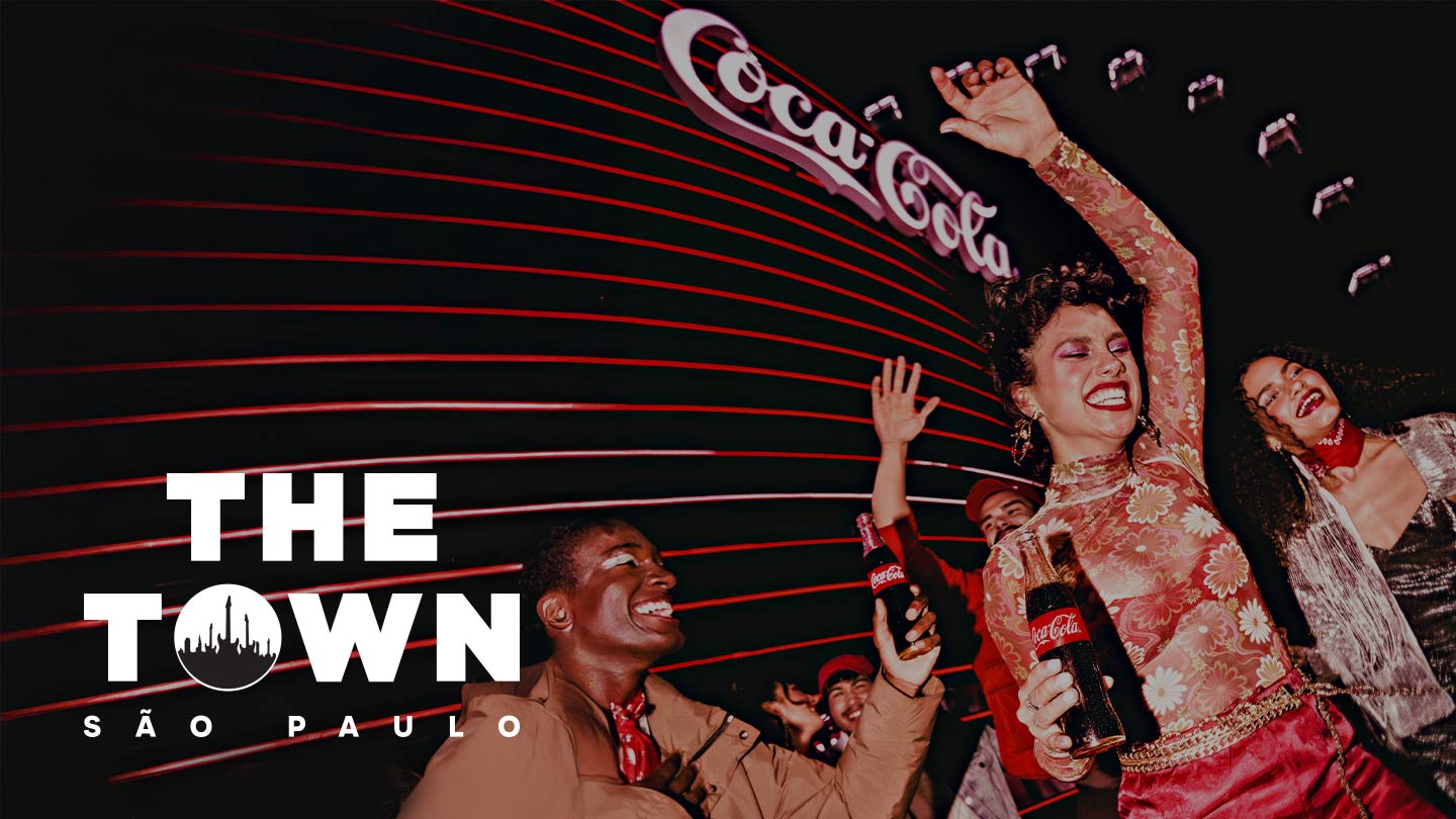 Imagem escura com o logo da Coca-Cola e "THE TOWN SÃO PAULO" em destaque, mostrando pessoas animadas em um evento.