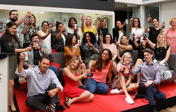 A group of employees gathered together celebrating and raising a toast with different Coca-Cola beverages