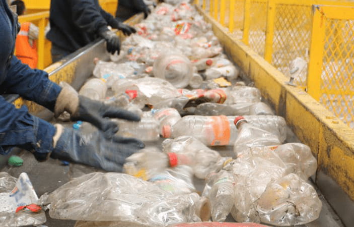 People working in a recycling sorting facility, going through plastic bottles