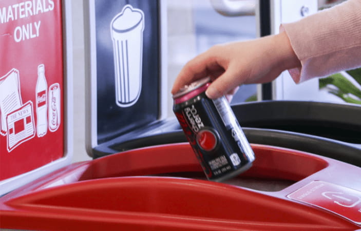 A woman's hand recycling a can of Coca-Cola