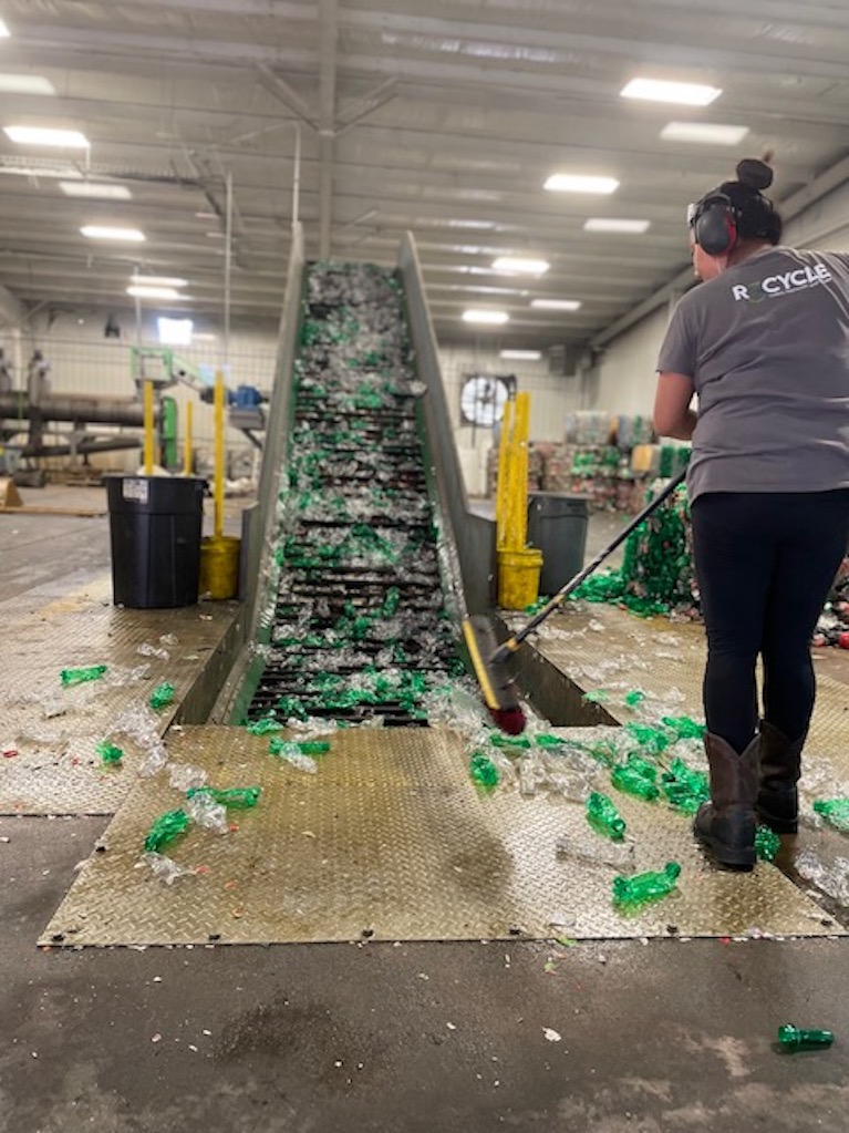 A woman sweeping empty plastic bottles on the floor of a plastic recycling facility