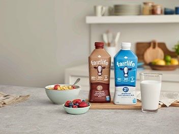 A fairlife® milk packaging, a glass of milk and a cereal bowl side by side