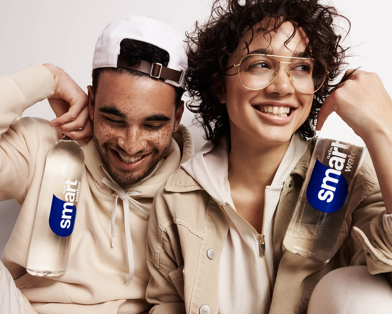 A man and woman smiling while holding bottles of smartwater.