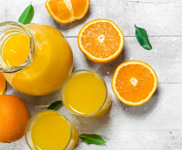 Top view a jar and two glasses of orange juice and a few sliced oranges on top of a table