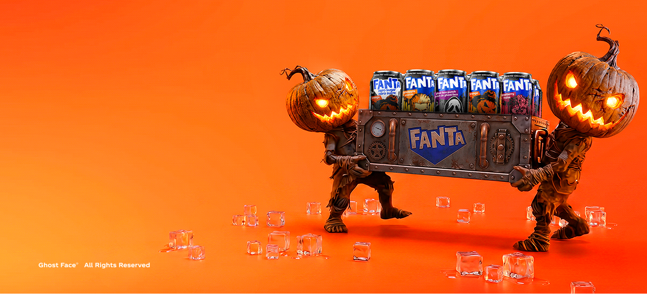 Two pumpkin-headed figures carry a metal Fanta crate filled with monster-themed Halloween cans on an orange background.