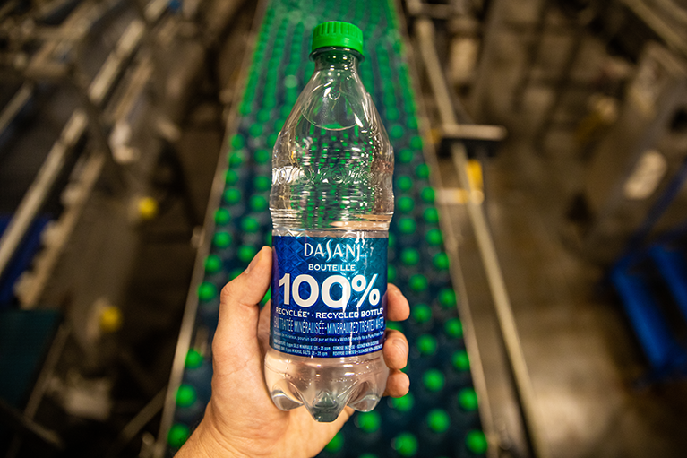 Un homme montre une bouteille d'eau DASANI 100% recyclable dans sa main