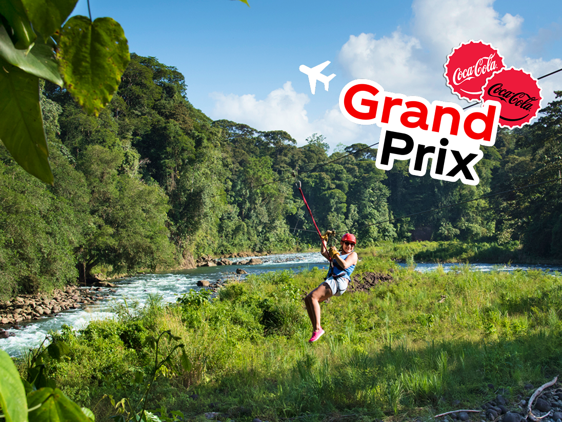 A hiker in a tropical rainforest stands on a cliff looking at the ocean. A colorful sticker with an airplane says, “Grand Prize.”