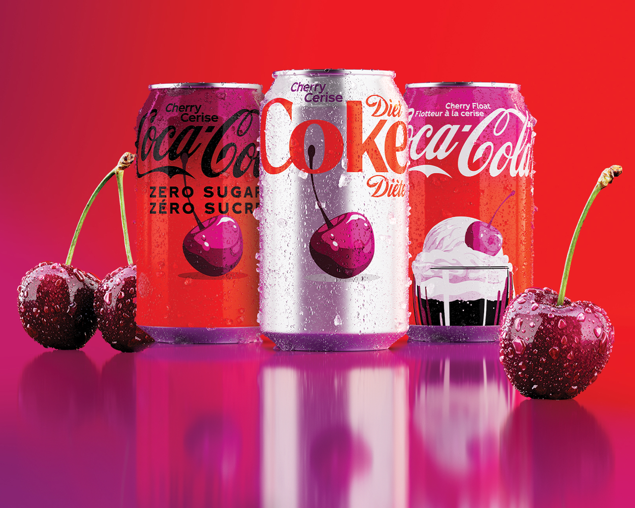 Trois canettes de Coca-Cola avec des étiquettes bilingues anglais-français — Coca-Cola Cerise Zero Sugar/Zéro sucre, Diet Coke Cherry/Cerise Diète et Coca-Cola Cherry Float/Flotteur à la cerise — disposées devant un fond rouge avec des cerises fraîches et des gouttes d'eau sur une surface réfléchissante violet-rose.