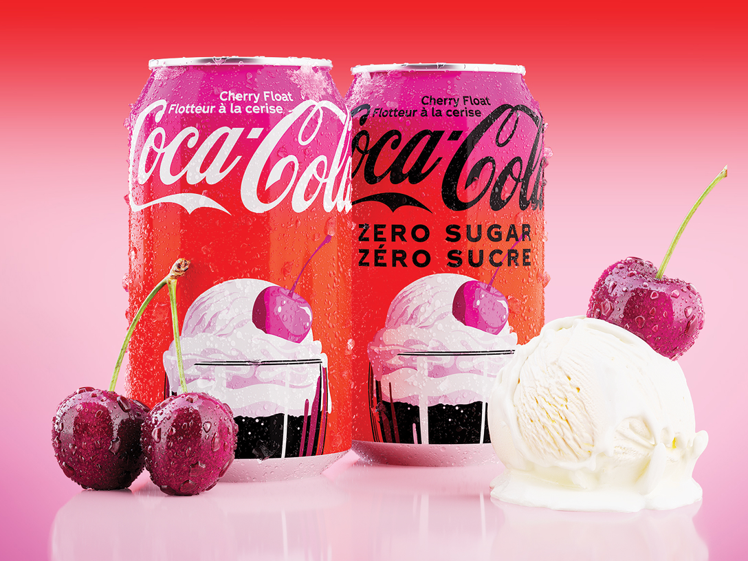 Deux canettes de Coca-Cola Flotteur à la cerise, l'une régulière et l'autre Zéro sucre, placées côte à côte sur un fond dégradé rouge et rose, accompagnées de cerises fraîches et d'une boule de crème glacée à la vanille.